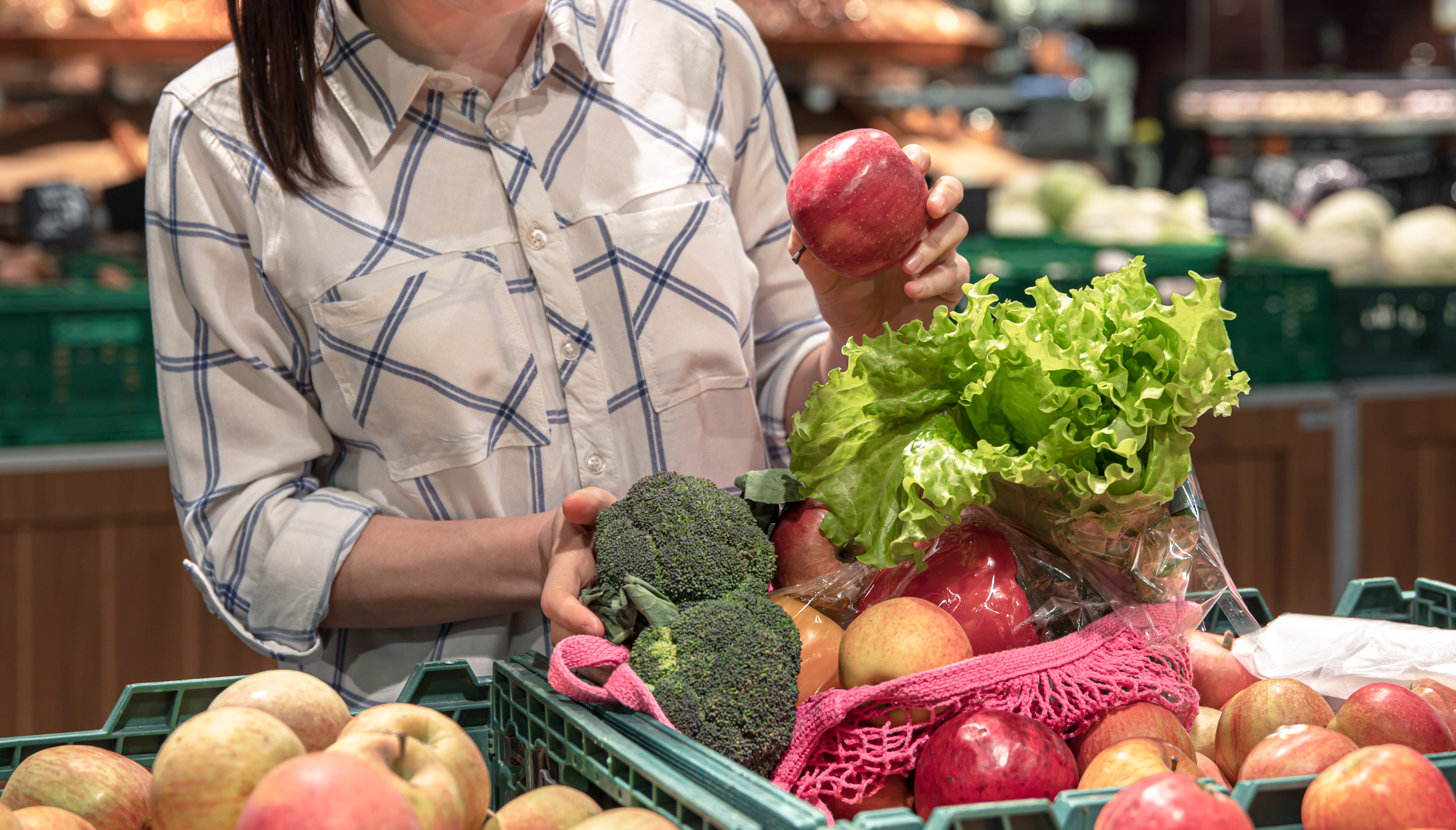Mulher no setor de frutas e legumes do supermercado, colocando alface e espinafre no carrinho com maçãs