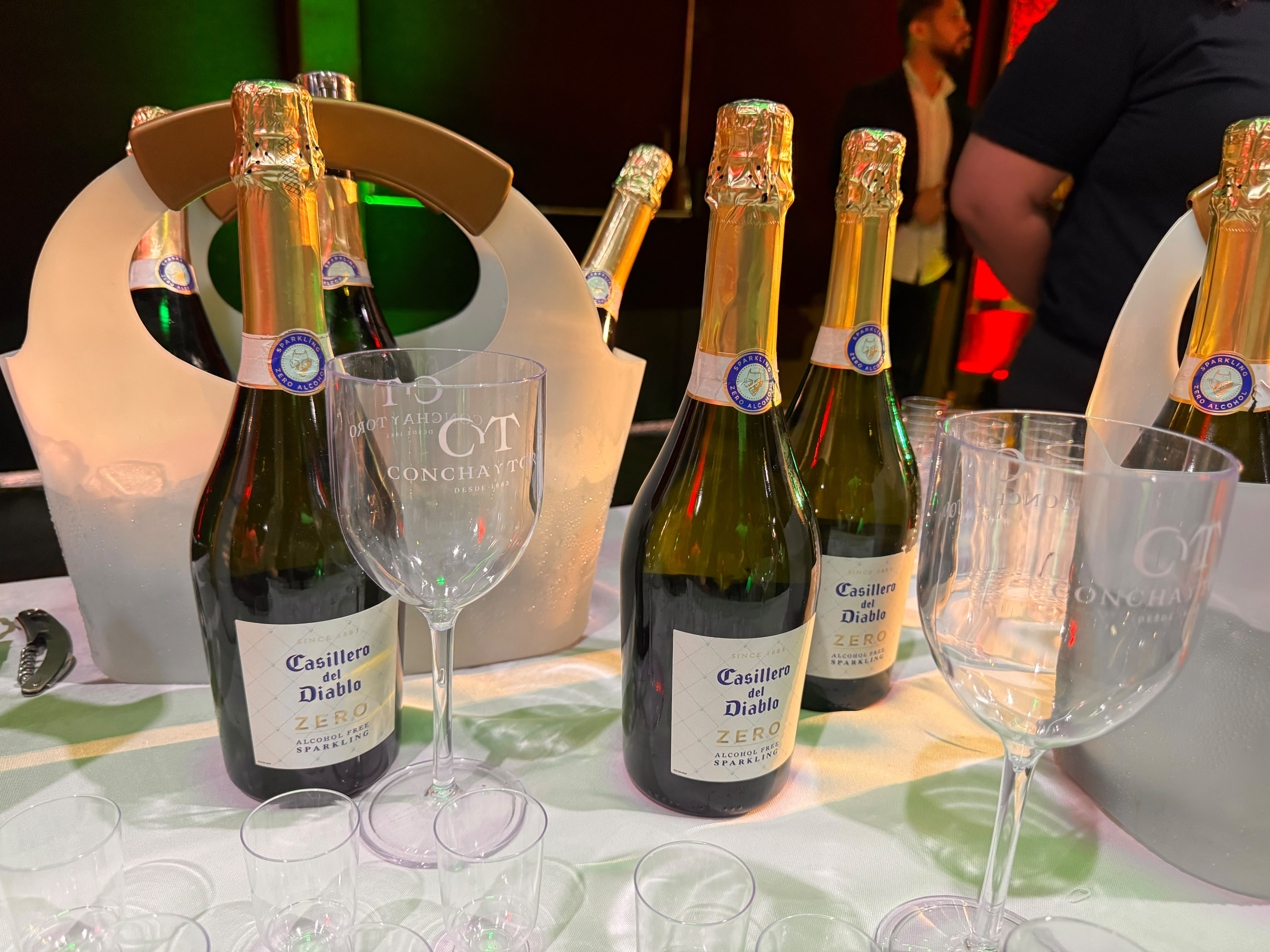 Mesa com garrafas de espumante Casillero Del Diablo Zero Álcool da Concha y Tora dispostas ao lado de taças 